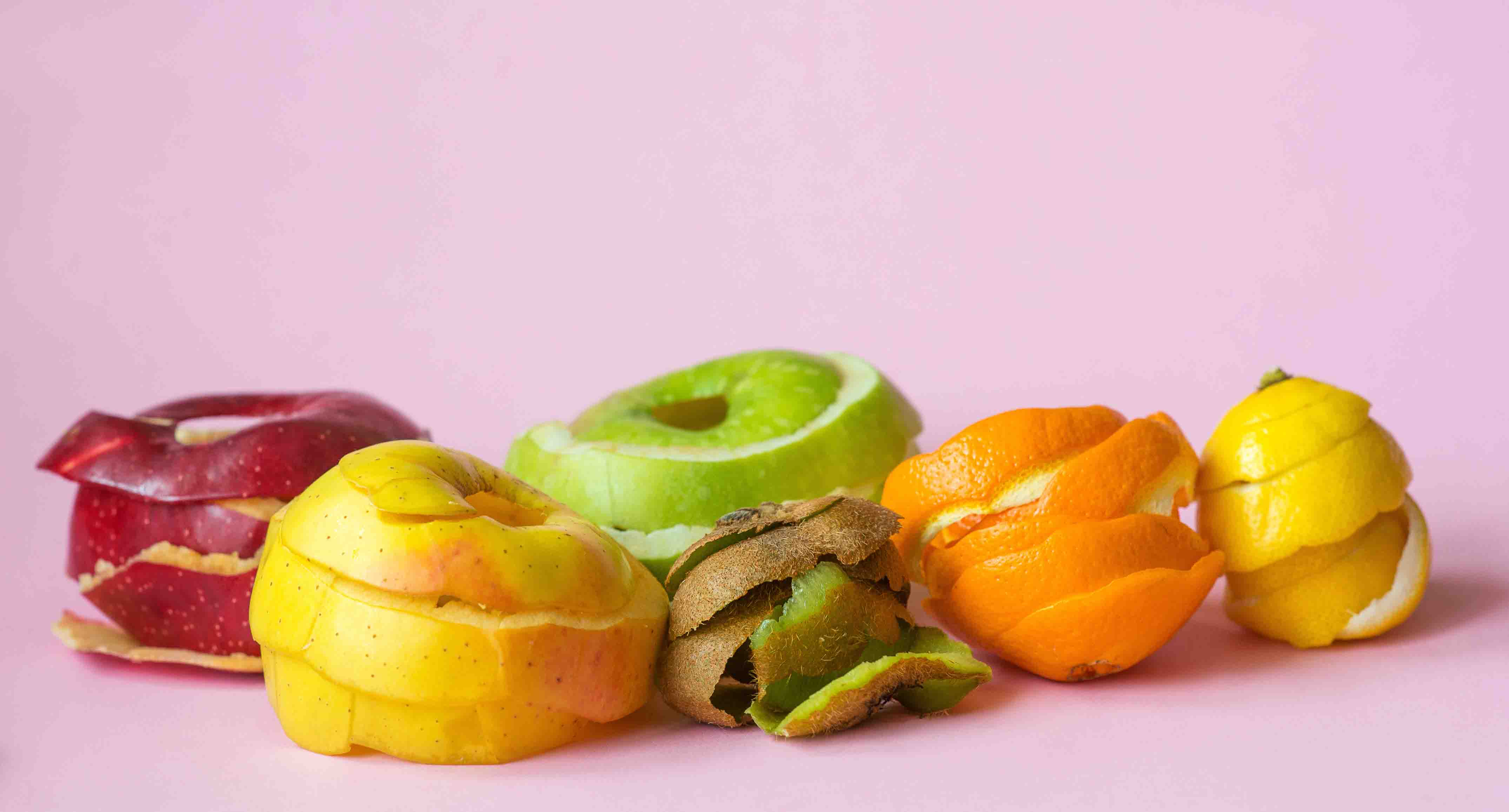 kiwi, orange, lemon and red, green, yellow apple peels on pink b