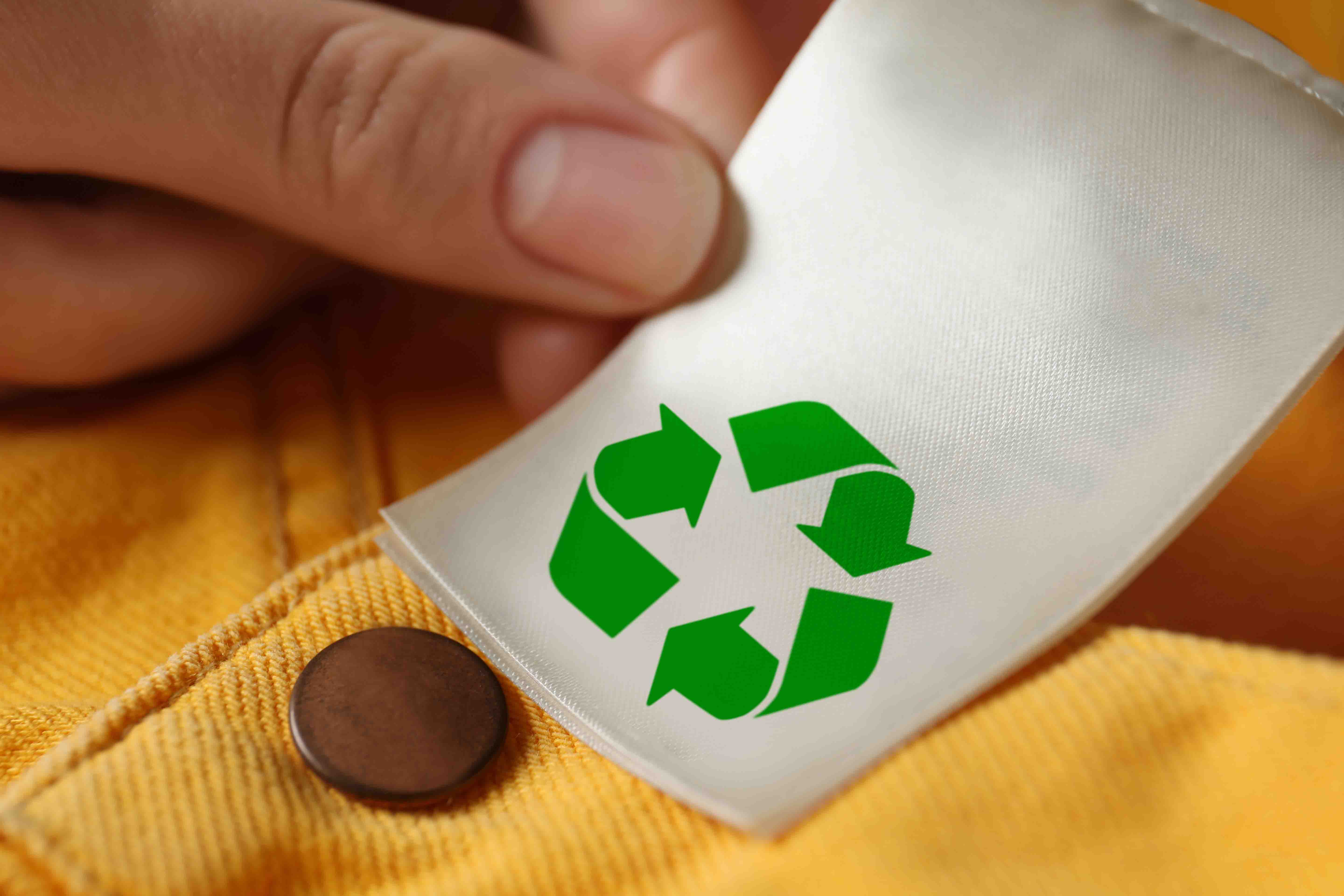Woman showing clothing label with recycling symbol on yellow jea