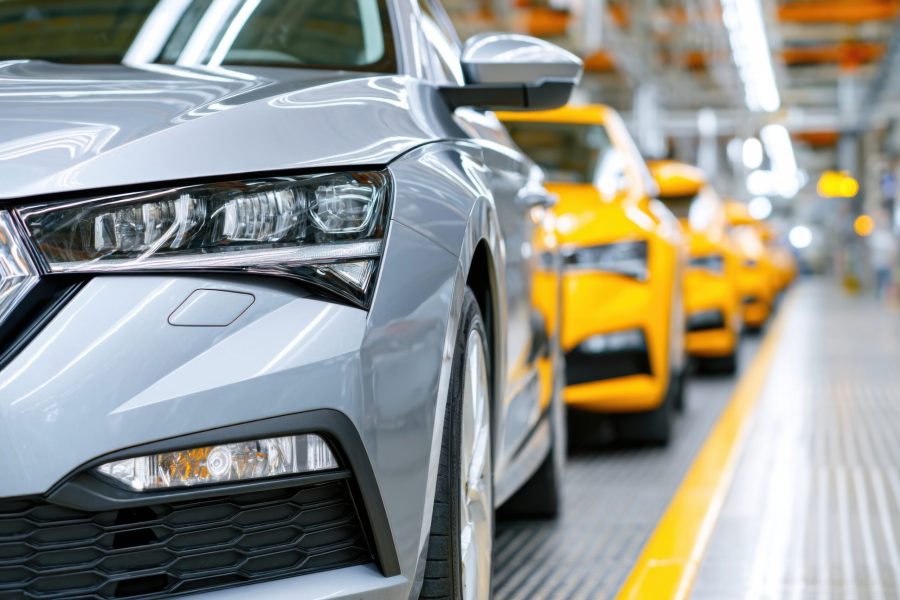 Silver sedan positioned in a contemporary automotive assembly line, displaying innovative design and technology, with bright yellow cars behind, emphasizing manufacturing processes