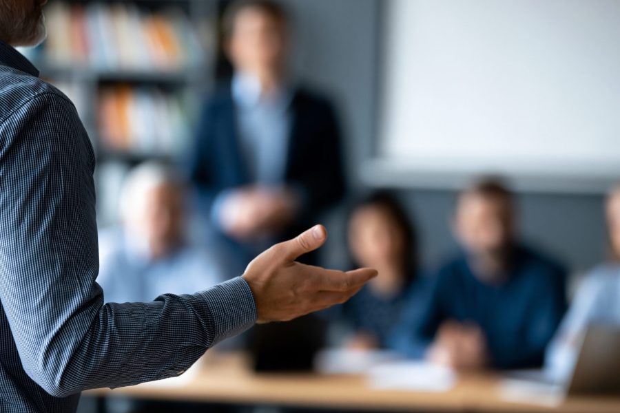 Faceless business trainer facilitating a leadership development workshop for a group of managers in a corporate training room, defocused training environment in background,