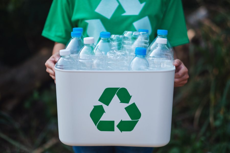 A woman collecting garbage and holding a recycle bin with plastic bottles in the outdoors