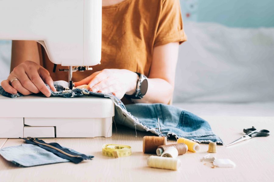 A woman tailor works at a sewing machine sews reuses fabric from old denim clothes. The concept of economical reuse of recyclable things. Homemade needlework hobby. Selective focus