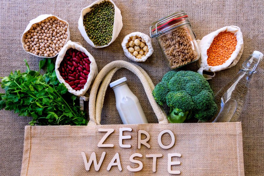 Ecological bag with inscription on burlap background. Reusable pouches with chickpeas, hazelnuts, beans, lentils, broccoli, parsley, glass bottles and jar are inside. Zero waste shopping concept.