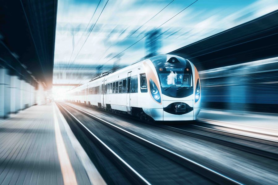 High speed train at the railway station at sunset in Europe. Modern intercity train on railway platform. Urban scene with beautiful passenger train on railroad and buildings. Railway landscape