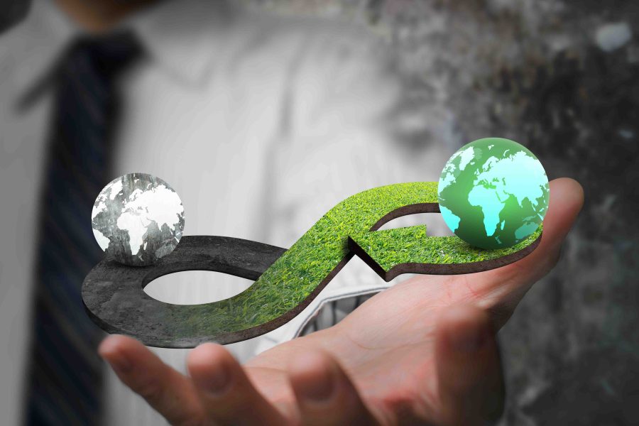 Green circular economy concept. Hand showing arrow infinity symbol with grass texture and two globes of different colors.